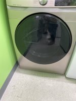 Front-loading washing machine with a cracked glass door against a lime-green wall. Control panel at the top is visible.