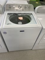 Whirlpool/MAYTAG top-load washing machine in a showroom with control panel on top and a sticky note inside the drum area.