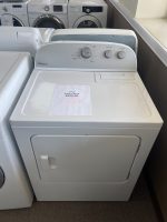 White Whirlpool top-load washer in a showroom with a sale price sheet on the lid, surrounded by other laundry machines in the background