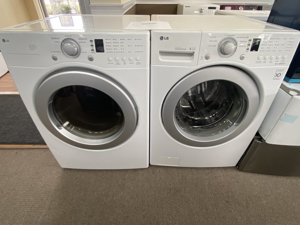Pair of LG front-loading washing machines in a showroom, white/silver, with control panels visible on top front.