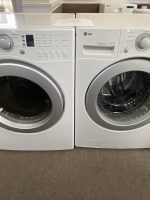 Pair of LG front-loading washing machines in a showroom, white/silver, with control panels visible on top front.