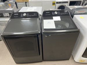 Pair of black Samsung top-load washing machines in a showroom with price tag visible on one unit