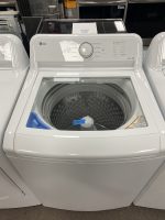 Front-loading LG washing machine in a showroom, with the door open and drum visible inside. Control panel and detergent drawer in view on the top panel.