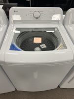 LG top-loading washing machine on display in a showroom, with a round control dial on the front panel and a price note taped to the drum