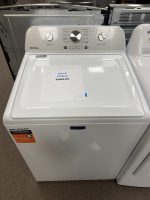 White Maytag top-load washing machine on showroom floor with a sale price sheet on the lid.
