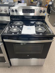 Black GE electric range with four coil burners in a showroom; sale price sheet resting on the cooktop.