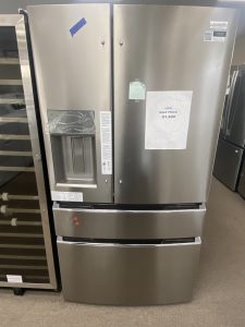 Stainless steel French-door fridge with water dispenser on the left, sale flyer taped to the right door showing $1,800.