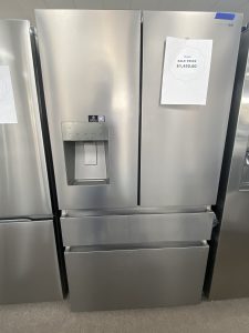 Side-by-side stainless steel refrigerator with a built-in water dispenser on the left door; a sale price tag is attached to the right door.