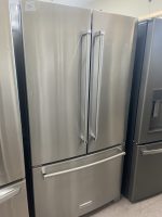 Stainless steel KitchenAid side-by-side refrigerator with two tall doors and long vertical handles in a showroom.