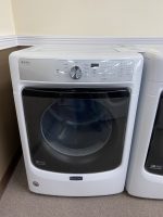 Front-loading Maytag washer with control panel and circular door in a laundry room corner.