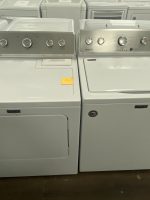 Row of white Maytag top-loading washing machines and dryers in a showroom.