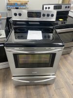 Freestanding stainless steel electric range with black ceramic cooktop and four burners, price sign on the surface in a showroom.